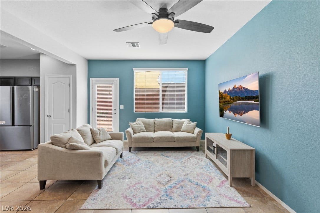 A vibrant living area features a refreshing blue accent wall, inviting comfortable sofas, and tiled flooring.