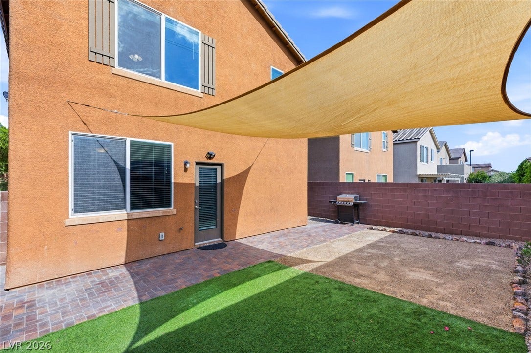 A private yard with artificial turf, a paver patio, and a sun shade for comfortable outdoor living.