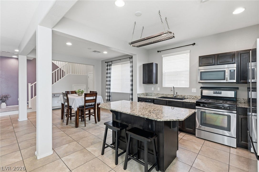 Granite counters and dark wood cabinetry define this well-appointed kitchen, ideal for entertaining with its open flow to the dining area and staircase beyond.