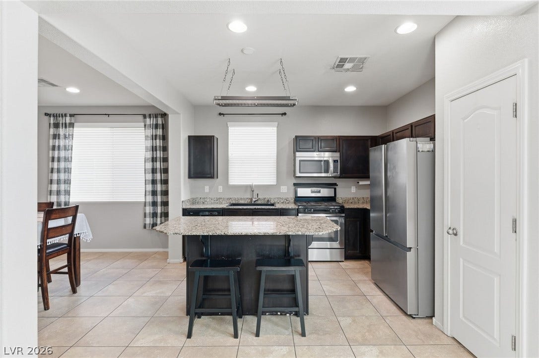 A contemporary kitchen and dining area feature granite countertops, stainless steel appliances, and tiled flooring.