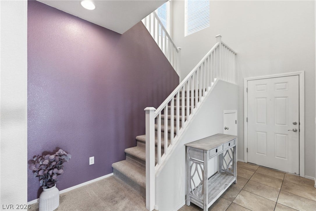 A welcoming entryway with a dual-level staircase, featuring both carpeted and tiled flooring, bathed in natural light.