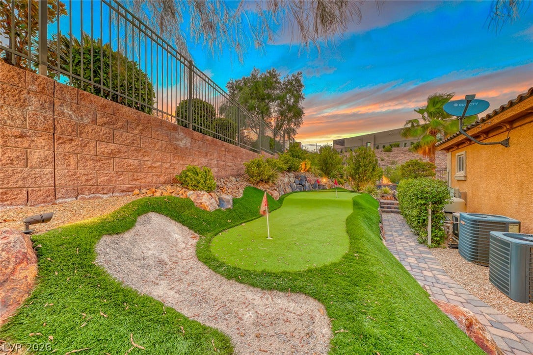 70 Portezza Drive, Henderson, NV 89011 An inviting backyard putting green with a sand trap awaits your short game practice under a vibrant sunset.