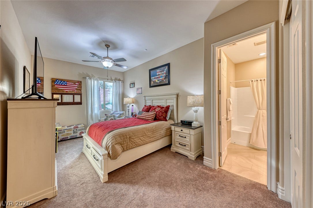 70 Portezza Drive, Henderson, NV 89011 Comfortable bedroom with neutral walls and soft carpeting, featuring a window and an adjacent bathroom.