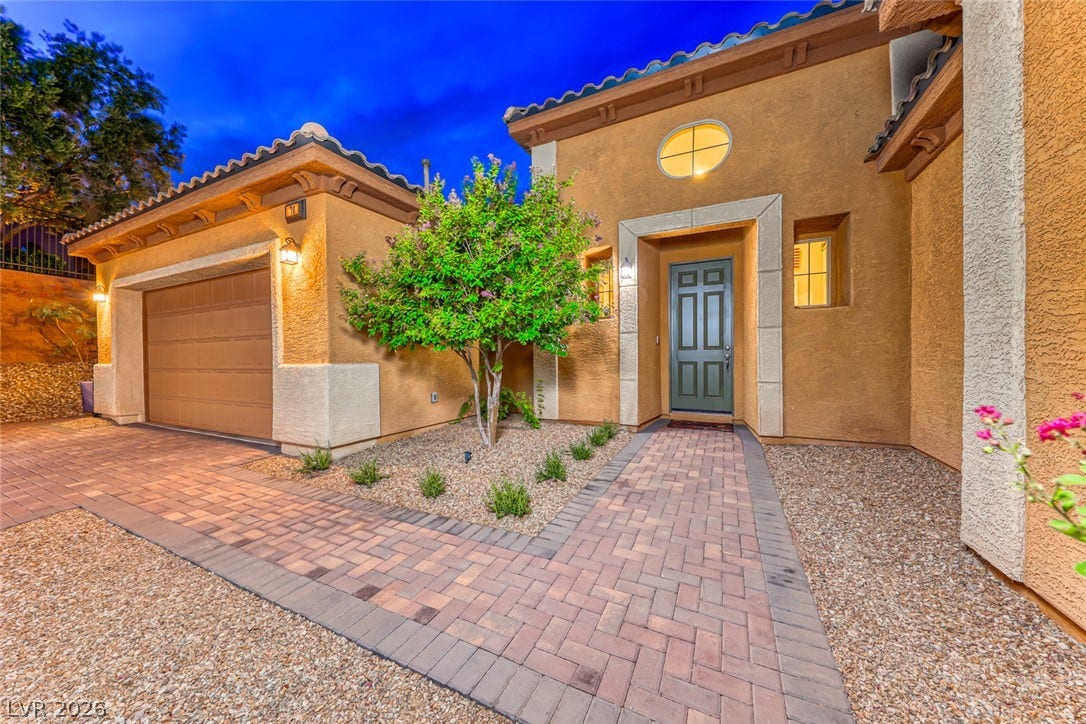 70 Portezza Drive, Henderson, NV 89011 A terracotta-hued stucco home presents a welcoming facade with a tiled entryway and a well-maintained paver driveway.