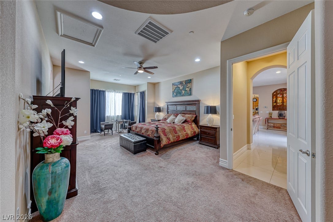 70 Portezza Drive, Henderson, NV 89011 A spacious primary bedroom retreat awaits, featuring plush carpeting and a charming sitting area by the window.