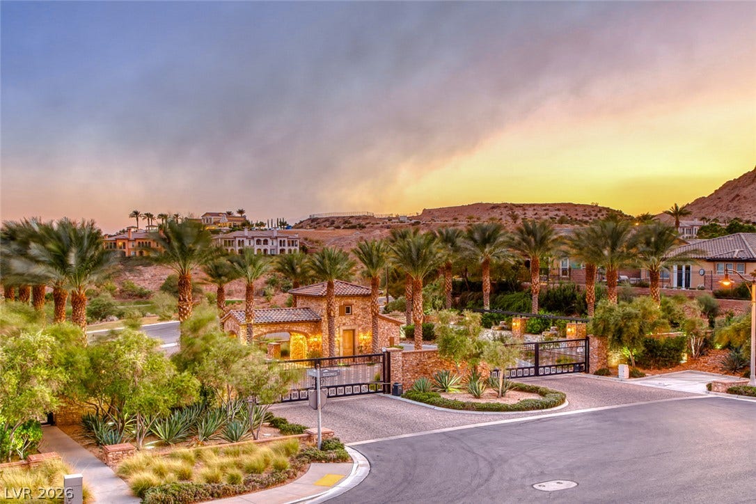 70 Portezza Drive, Henderson, NV 89011 A grand gated entrance welcomes residents to this luxurious desert community, featuring lush landscaping and distant hillside residences.