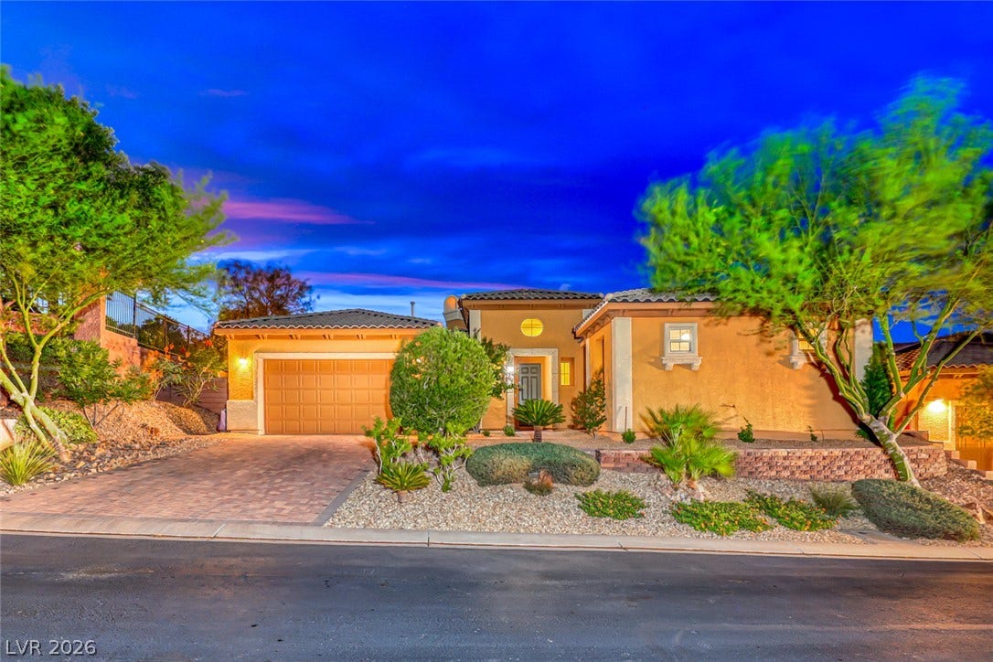 70 Portezza Drive, Henderson, NV 89011 A terracotta-hued residence features a tiled roof, paver driveway, and desert-inspired landscaping under a twilight sky.