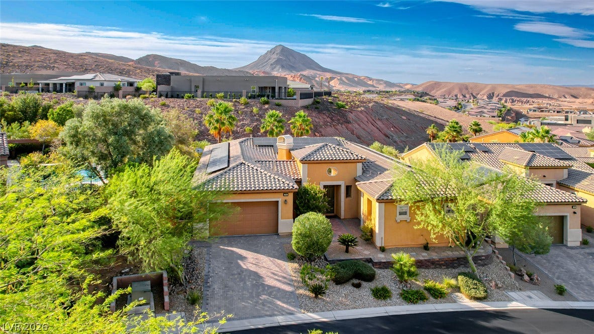 70 Portezza Drive, Henderson, NV 89011 An inviting exterior with desert-friendly landscaping, a paved driveway, and solar panels, set against a mountainous backdrop.