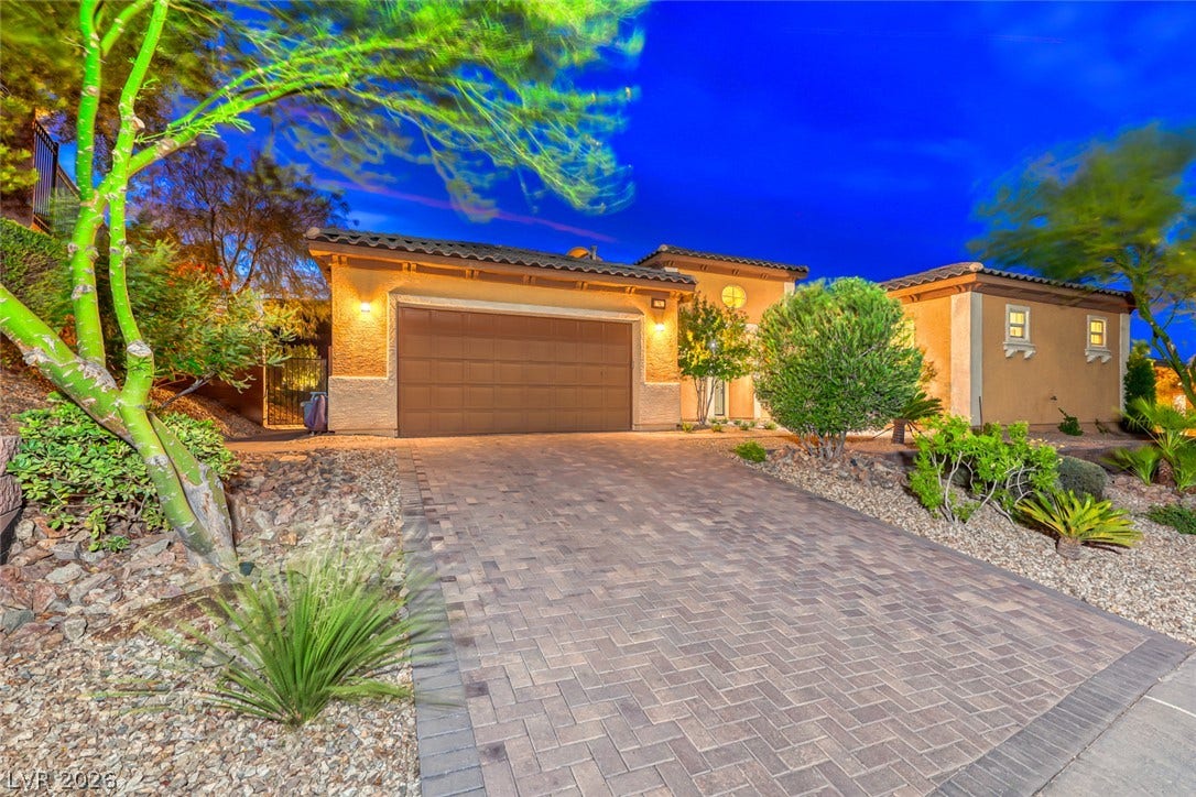 70 Portezza Drive, Henderson, NV 89011 A striking property with a brick paver driveway and desert-inspired landscaping, illuminated against a twilight sky.