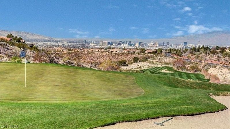 Green fairways stretch towards a distant city skyline, framed by rugged desert hills.