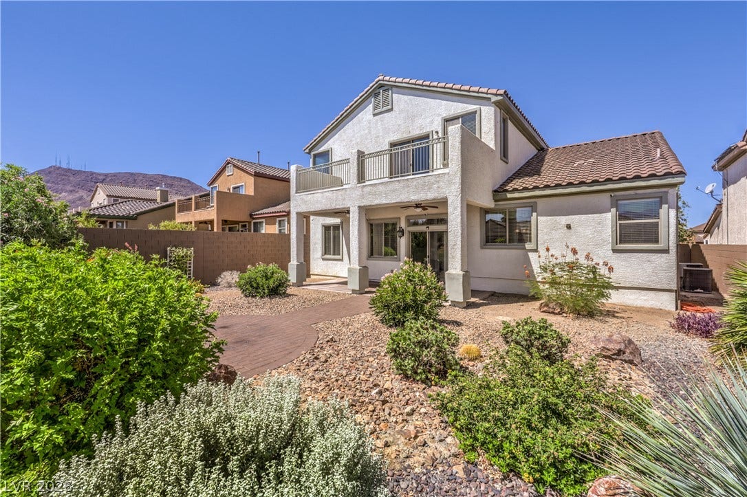 260 Quail Ranch Drive, Henderson, NV 89015 A spacious backyard with desert landscaping offers an upper balcony and a shaded patio beneath, perfect for outdoor enjoyment.