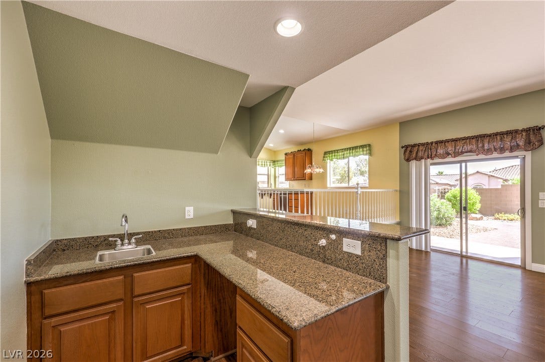 260 Quail Ranch Drive, Henderson, NV 89015 A well-appointed wet bar area, complete with granite countertops and rich wood cabinetry, opens to a bright adjacent living space and outdoor patio.