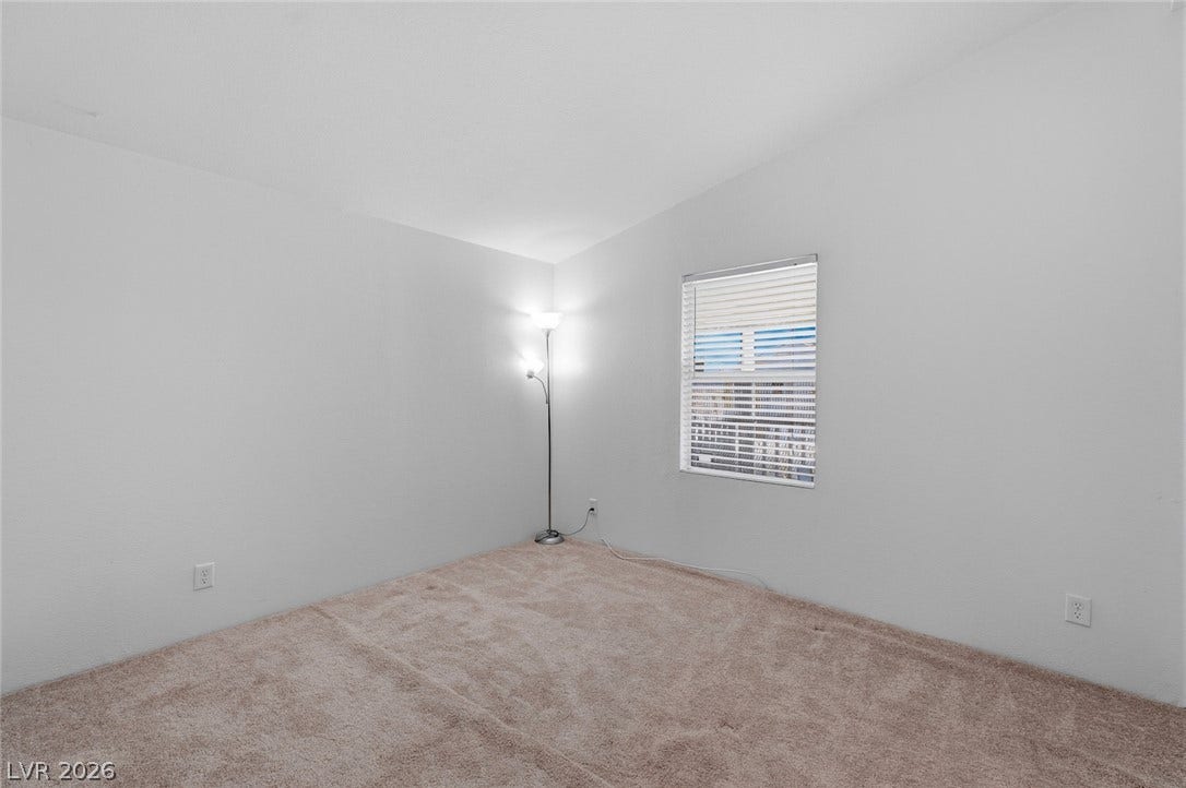 4589 Royal Ridge Boulevard, Las Vegas, NV 89103 A well-lit bedroom features plush carpeting and a window with blinds, creating a comfortable atmosphere.