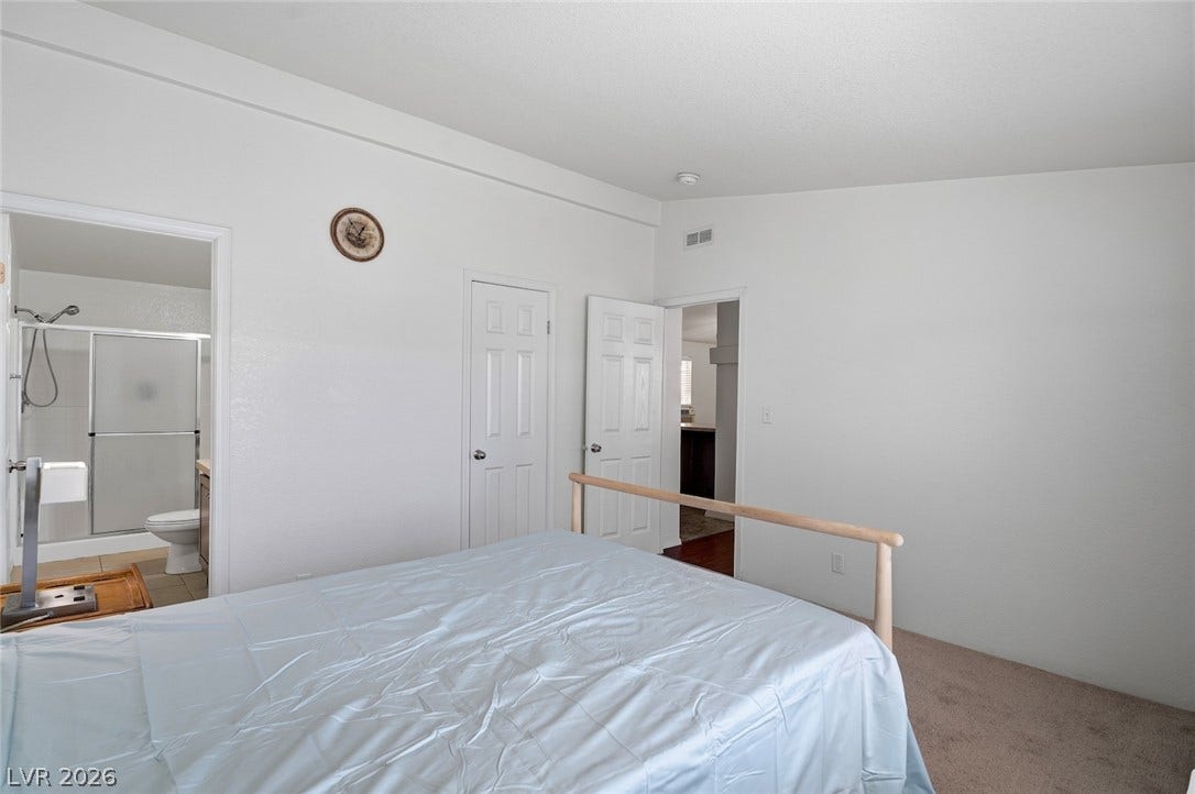 4589 Royal Ridge Boulevard, Las Vegas, NV 89103 A well-lit bedroom features plush carpeting and an adjoining bathroom, providing comfort and convenience.