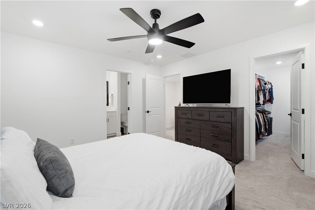 A well-lit bedroom features plush carpeting, a modern ceiling fan, and convenient access to an en-suite bathroom and walk-in closet.