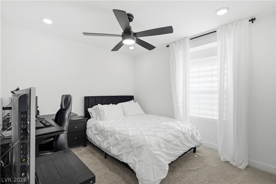 A well-lit sleeping area features recessed lighting, a modern ceiling fan, and soft, neutral-toned carpeting.