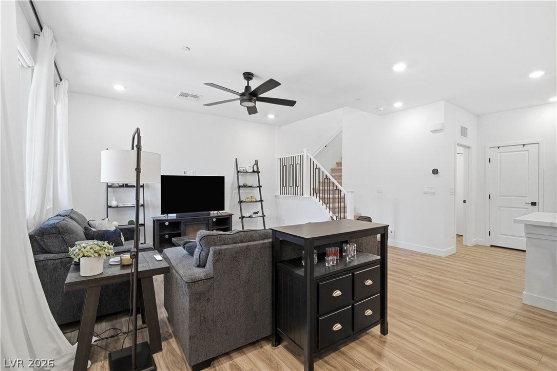 A contemporary living room features wood flooring, recessed lighting, and a staircase with sleek iron railings.