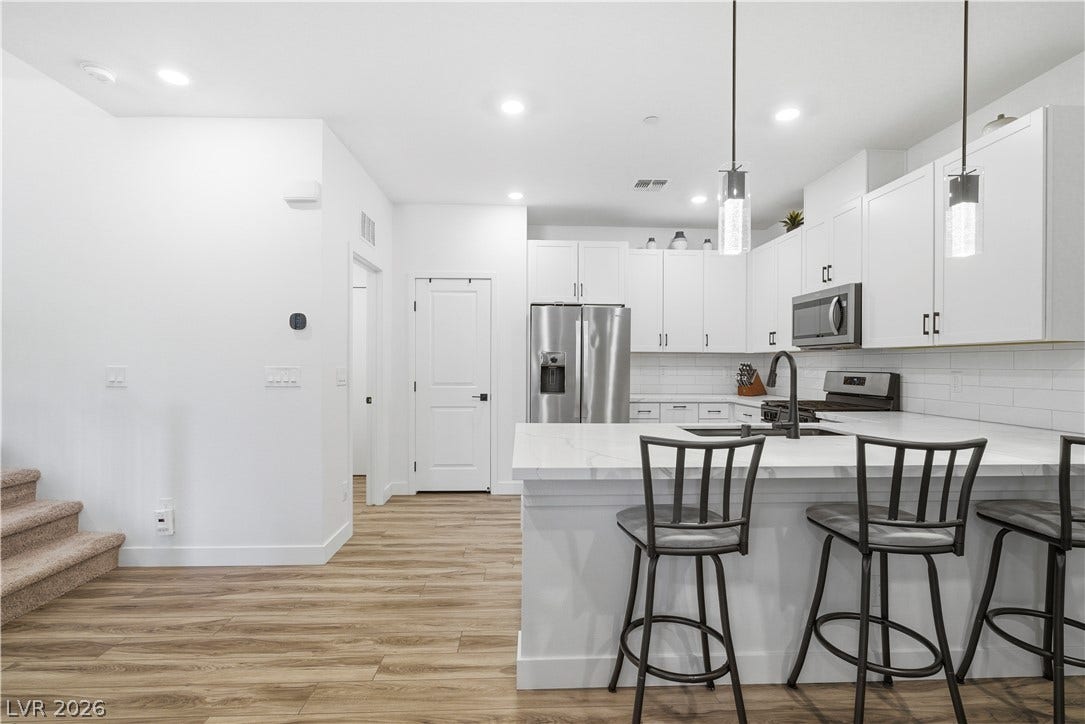 A contemporary kitchen space boasts sleek white cabinetry, stainless steel appliances, and wood-look flooring.