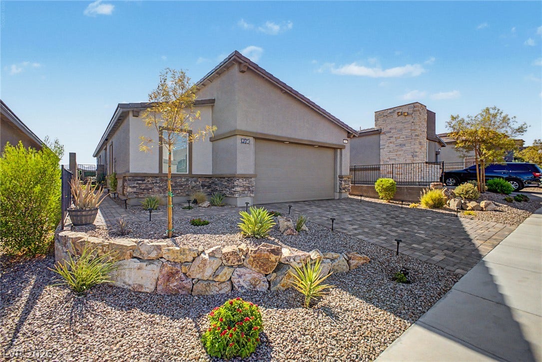 290 Fossil Falls Street, Henderson, NV 89015 A meticulously maintained front yard features desert-friendly landscaping, a stone retaining wall, and a paver driveway leading to an attached garage.