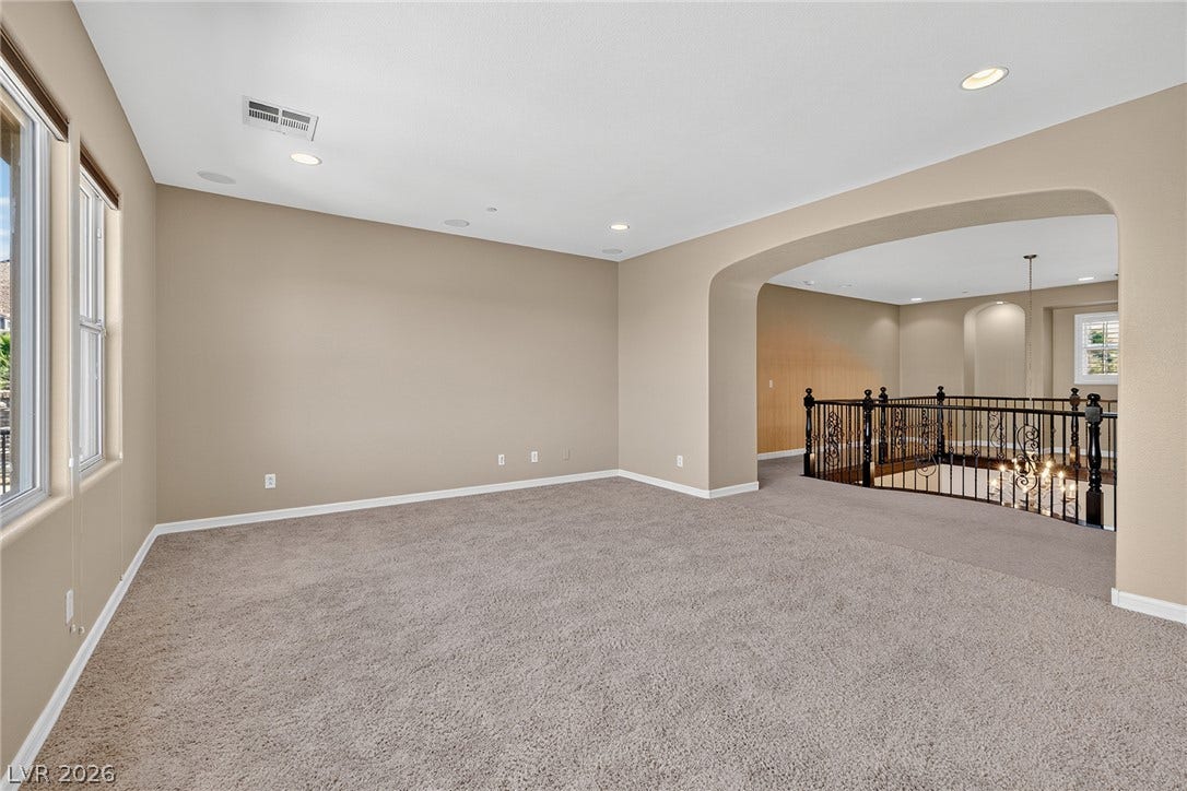 30 Benevolo Drive, Henderson, NV 89011 A spacious carpeted living area features an arched entryway, recessed lighting, and a wrought iron banister overlooking the floor below.