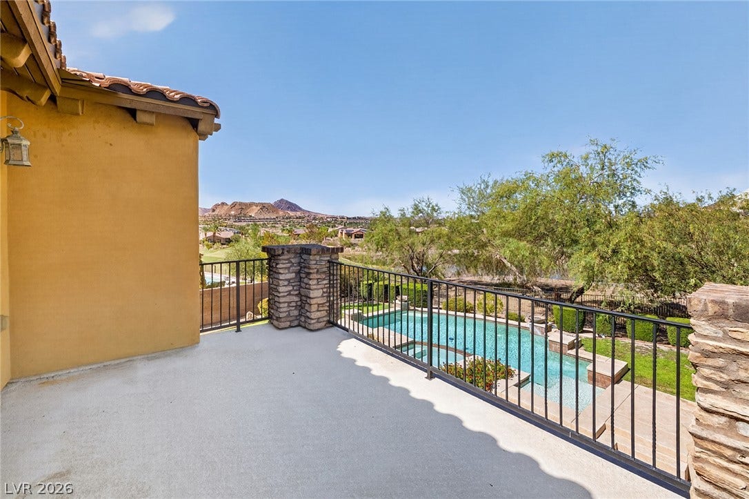 30 Benevolo Drive, Henderson, NV 89011 An inviting balcony overlooks a pristine pool, lush greenery, and distant mountains under an expansive sky.