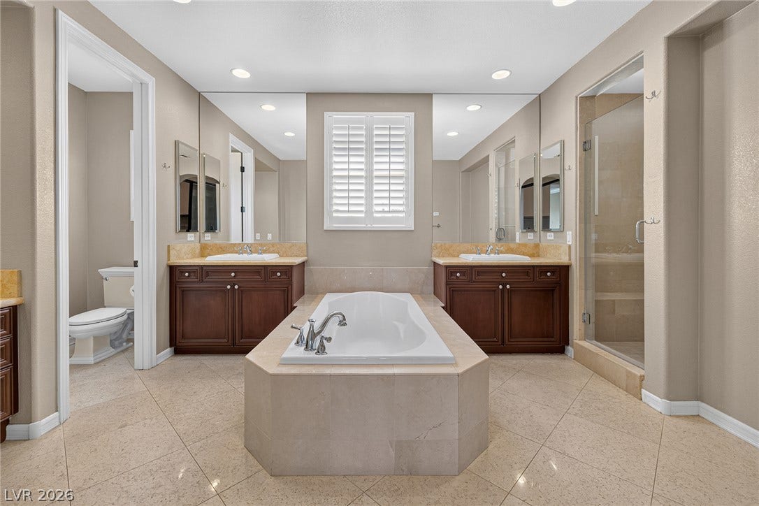 30 Benevolo Drive, Henderson, NV 89011 Indulge in a tranquil bathing experience within this bathroom's elegant, built-in soaking tub, complemented by dual vanities and a glass-enclosed shower.