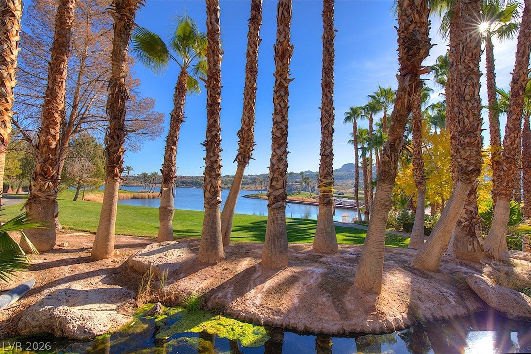 30 Benevolo Drive, Henderson, NV 89011 A tranquil lakefront property featuring mature palm trees and verdant landscaping, offering picturesque water and mountain vistas.