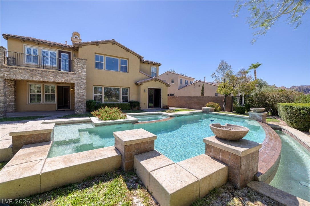 30 Benevolo Drive, Henderson, NV 89011 An inviting backyard oasis offers a sparkling pool with integrated spa and decorative fire bowls, set against a two-story home with a private balcony.