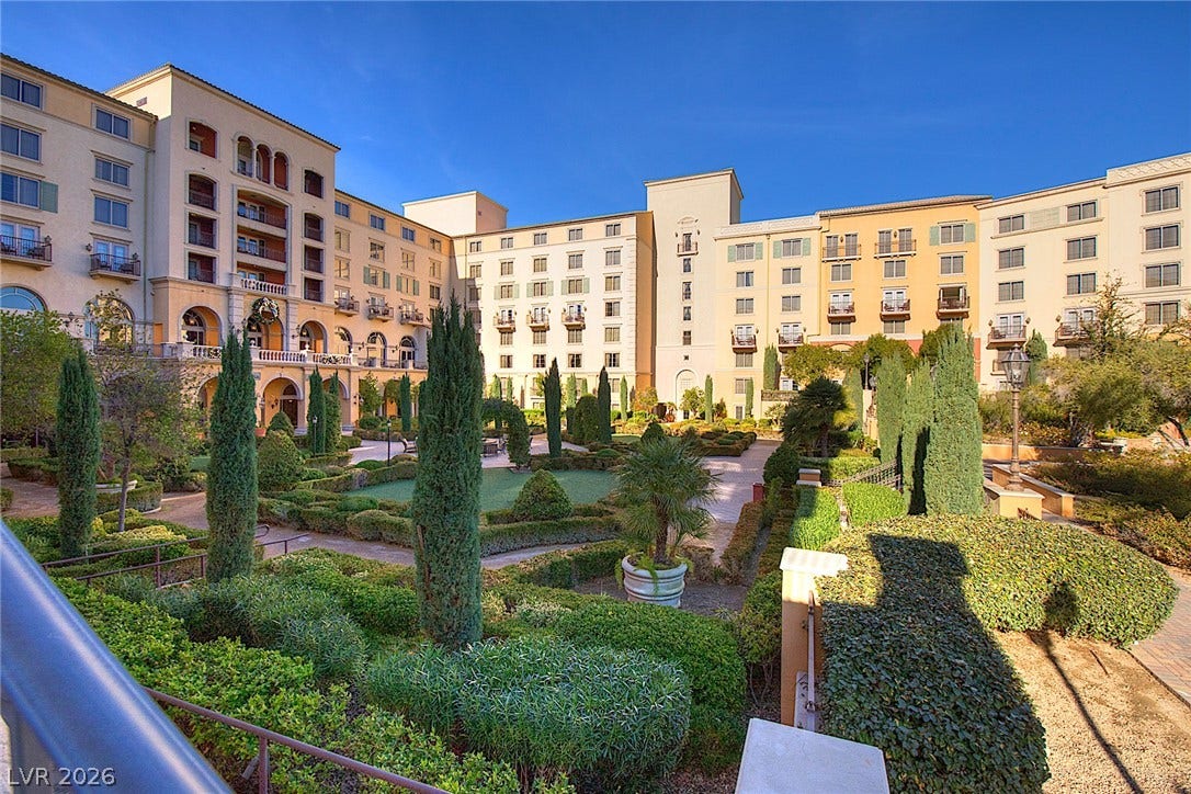 30 Benevolo Drive, Henderson, NV 89011 Ornate hedges and towering cypresses sculpt a grand courtyard garden, offering a serene escape within this elegant multi-story building complex.