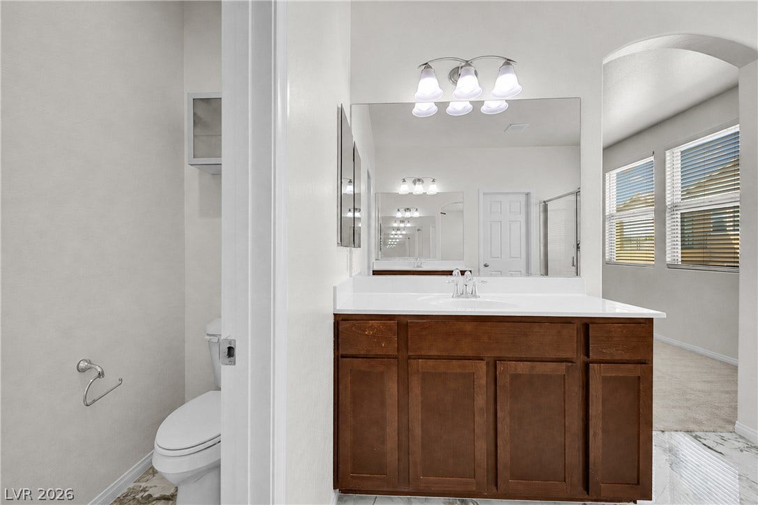 771 White Dogwood Court, Las Vegas, NV 89148 A pristine bathroom vanity, showcasing rich wood cabinetry and a spacious mirror, complements the room's elegant flooring.