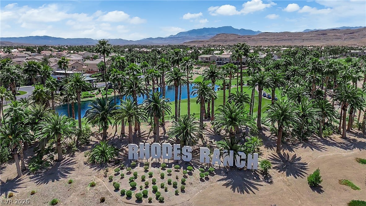 771 White Dogwood Court, Las Vegas, NV 89148 An aerial perspective reveals a lush golf course with mature palm trees and a serene lake, framed by residential homes and distant mountains.