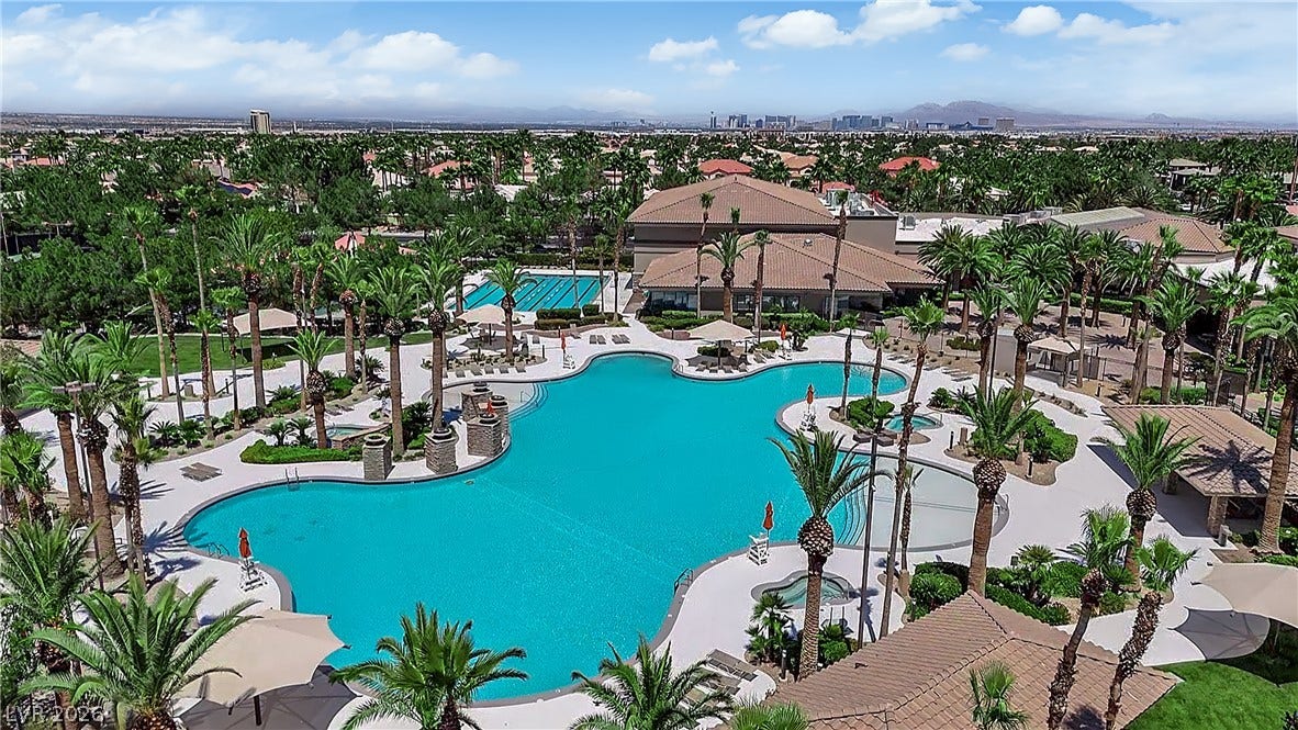771 White Dogwood Court, Las Vegas, NV 89148 An aerial perspective reveals a resort-style aquatic playground, featuring multiple pools amid lush palm trees and distant city views.