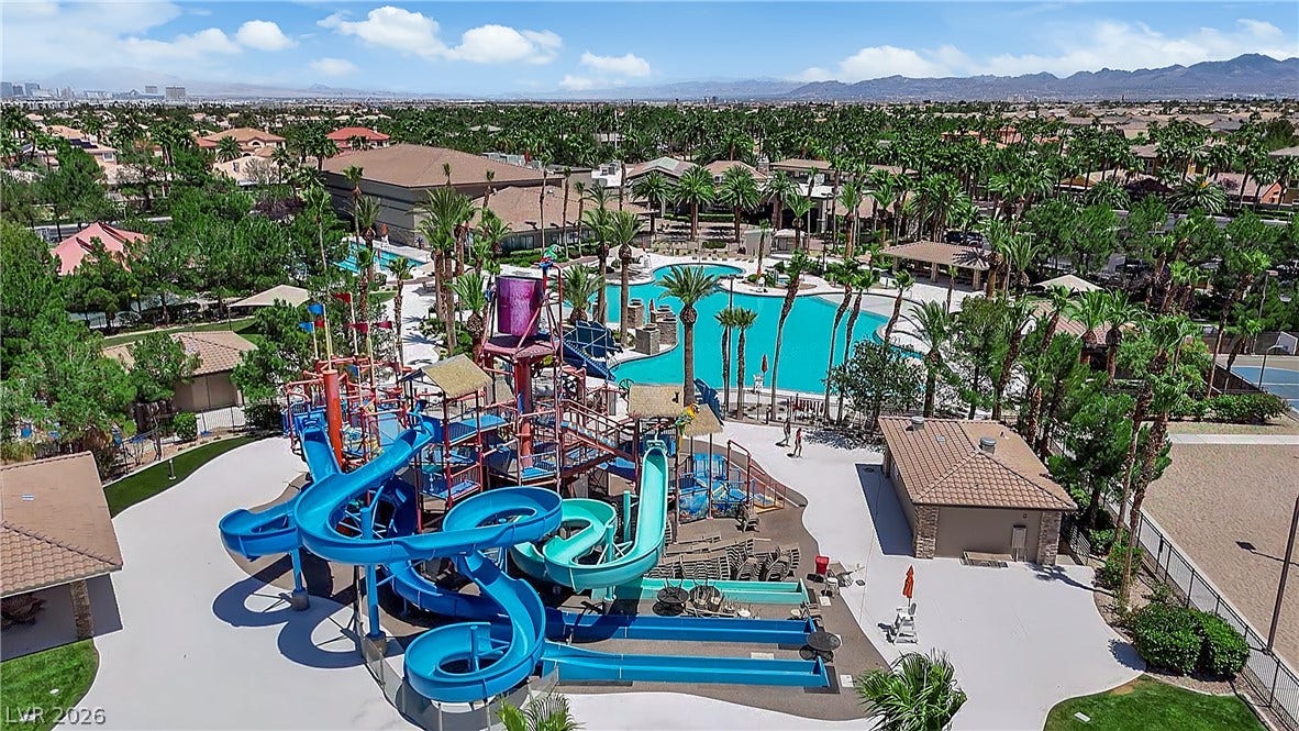 771 White Dogwood Court, Las Vegas, NV 89148 An aerial perspective reveals a vibrant community pool area with numerous slides, shaded lounging, and mature palm trees.