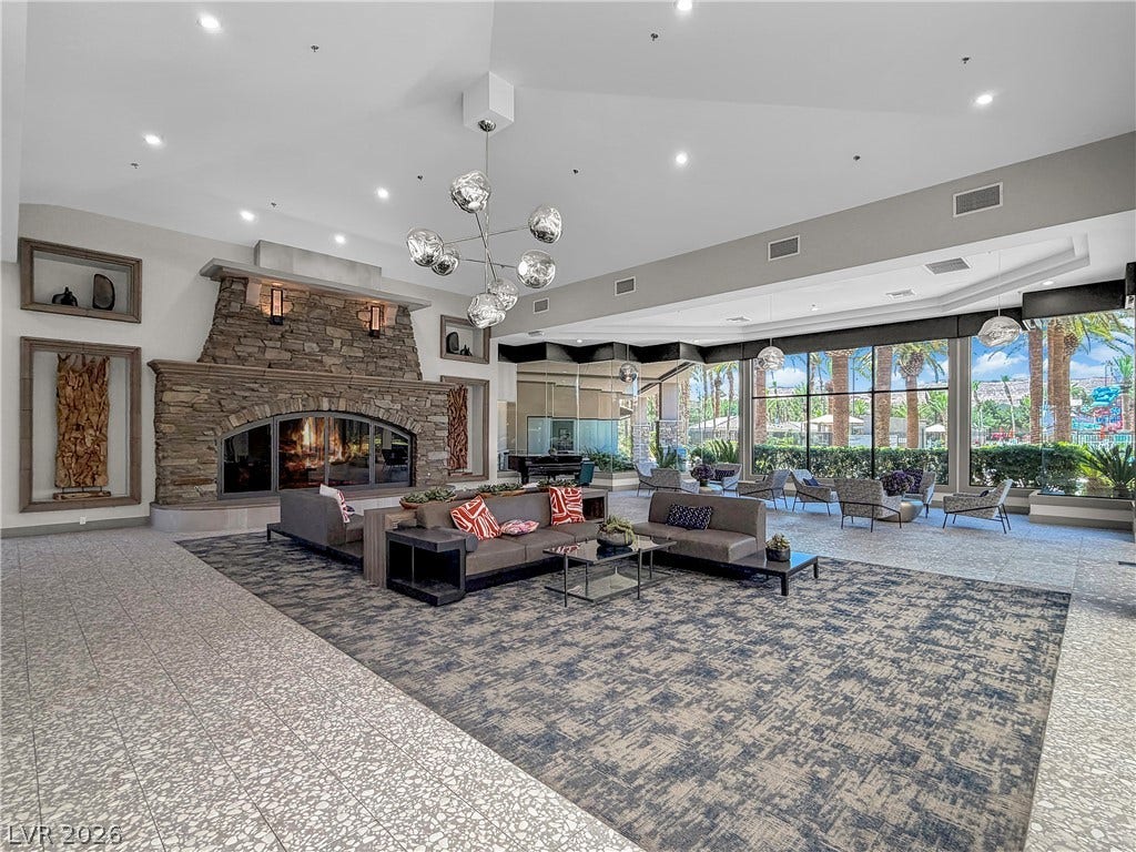 771 White Dogwood Court, Las Vegas, NV 89148 An inviting gathering space features a stone-clad fireplace and abundant natural light from expansive windows overlooking tropical foliage.