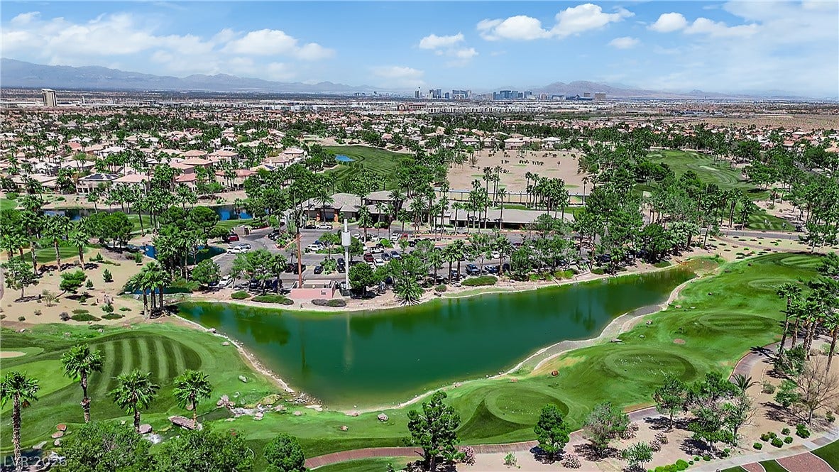 771 White Dogwood Court, Las Vegas, NV 89148 An aerial panorama reveals a verdant golf course community surrounding a tranquil lake, set against a distant cityscape.
