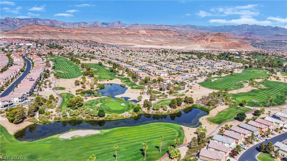 771 White Dogwood Court, Las Vegas, NV 89148 An aerial perspective reveals a vibrant golf course community nestled against a striking mountain backdrop, featuring tranquil water hazards.