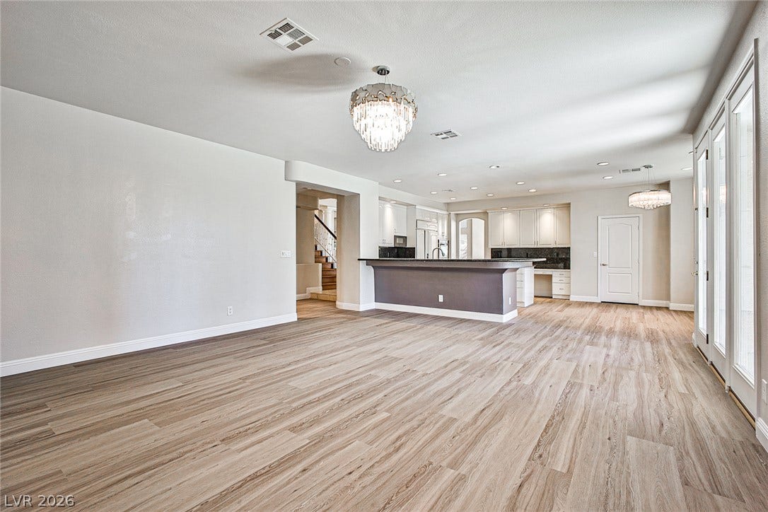 1828 Dolce Drive, Las Vegas, NV 89134 A spacious great room unfolds with light wood-look flooring and a modern chandelier, flowing seamlessly into a well-appointed kitchen.