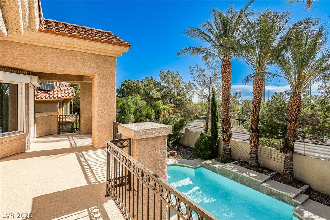 1828 Dolce Drive, Las Vegas, NV 89134 An inviting balcony overlooks a private plunge pool, embraced by vibrant greenery and swaying palm trees.