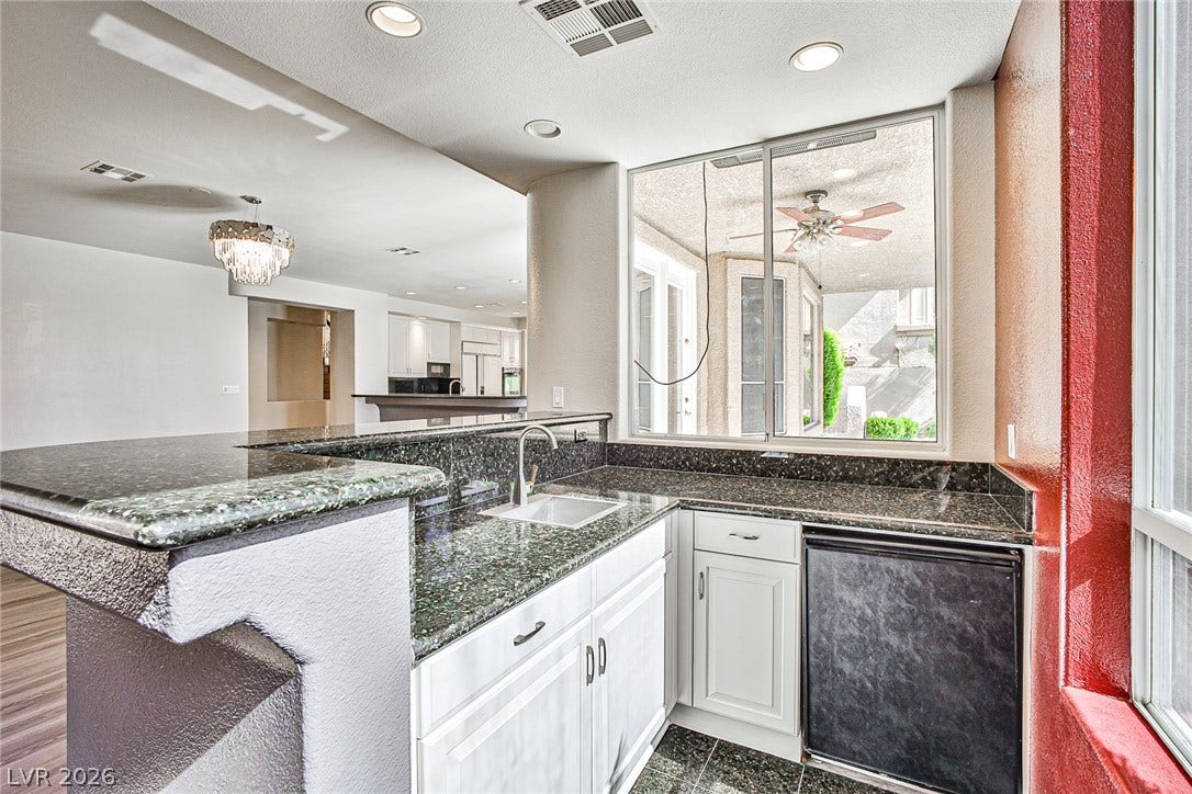 1828 Dolce Drive, Las Vegas, NV 89134 A well-appointed kitchen features dark granite counters, white cabinetry, and an integrated mini-fridge beneath a wide window.