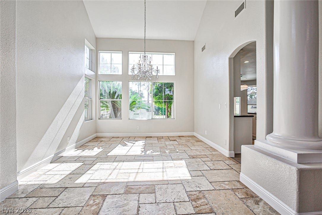 1828 Dolce Drive, Las Vegas, NV 89134 Natural light floods this spacious living area, highlighting vaulted ceilings and stone tile flooring, with a glimpse into the adjoining kitchen.