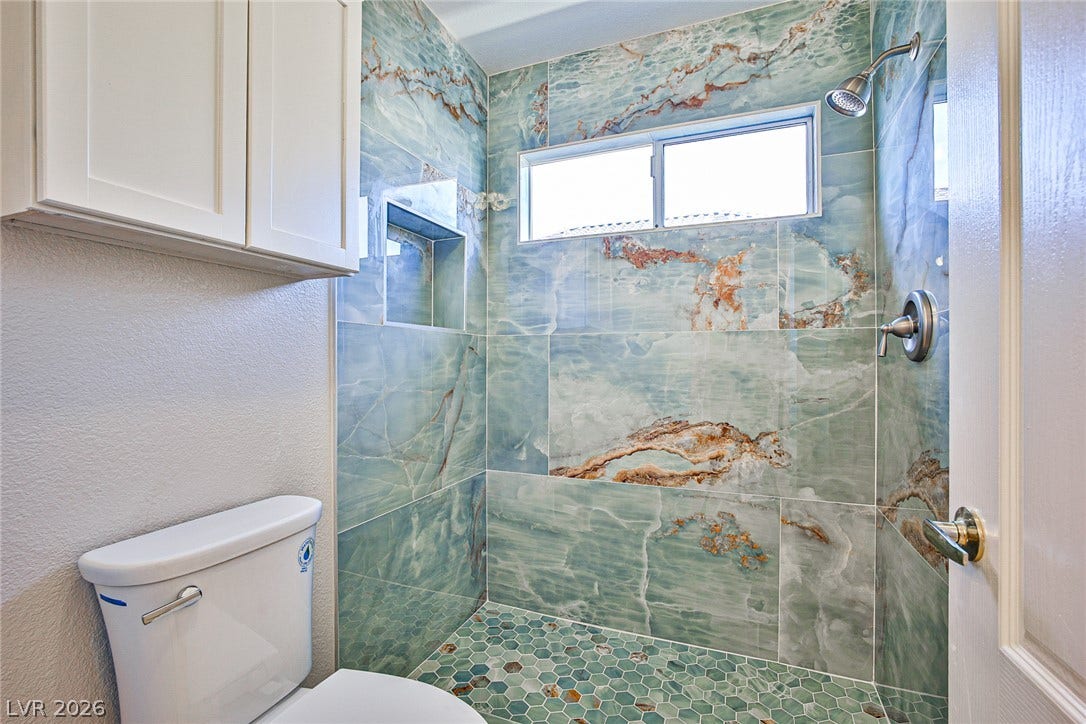 1828 Dolce Drive, Las Vegas, NV 89134 A stylish shower area features striking blue and rust-toned tile work with a complementary hexagonal floor.