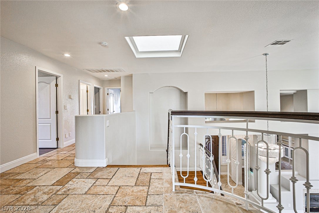 1828 Dolce Drive, Las Vegas, NV 89134 Natural light floods this inviting hallway, showcasing elegant tile flooring and a distinctive wrought iron stair railing.