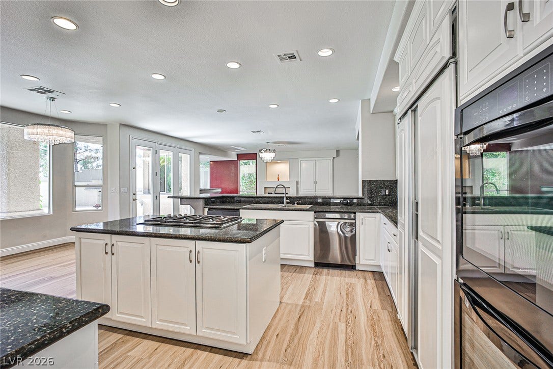 1828 Dolce Drive, Las Vegas, NV 89134 An open-concept kitchen features bright cabinetry and speckled granite countertops, alongside a central island with a gas cooktop.