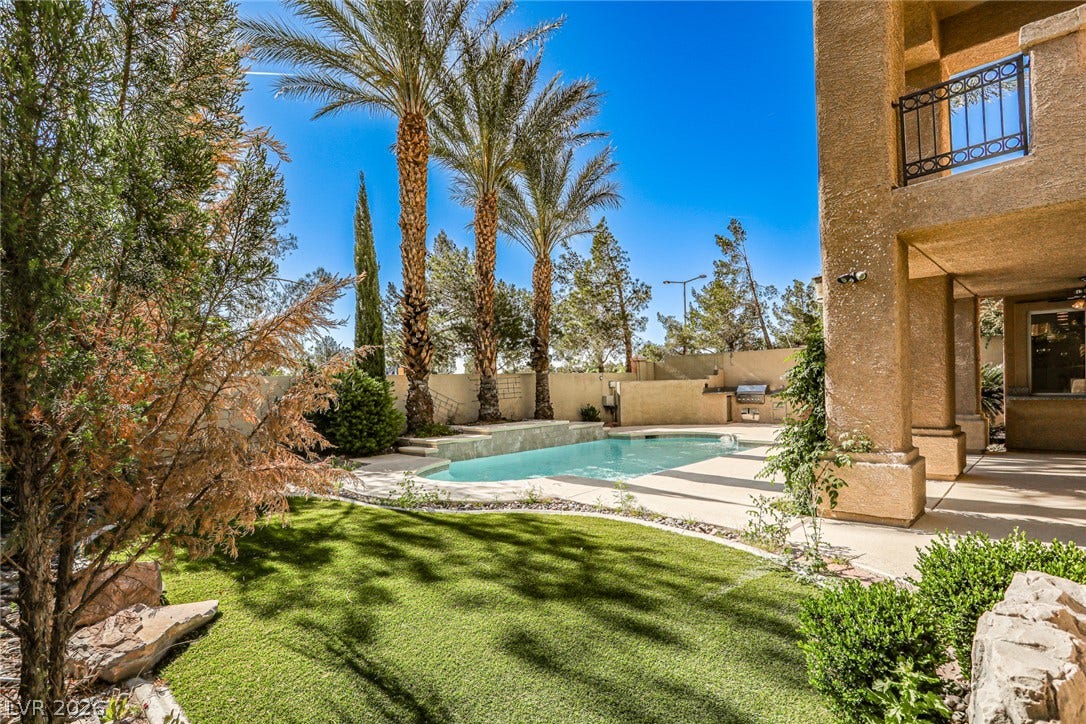 1828 Dolce Drive, Las Vegas, NV 89134 A tranquil backyard oasis presents a refreshing pool, lush green turf, and established palm trees.