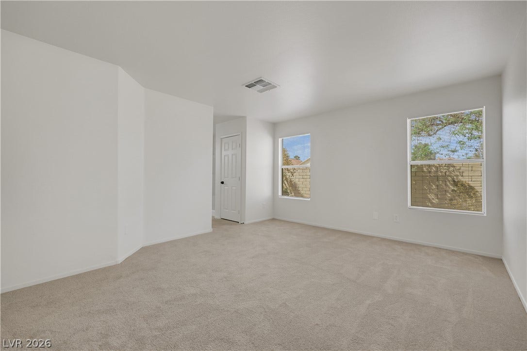 648 Moonlight Mesa Drive, Henderson, NV 89011 A spacious and inviting room with plush carpeting, two windows offering natural light, and a clean, neutral palette.