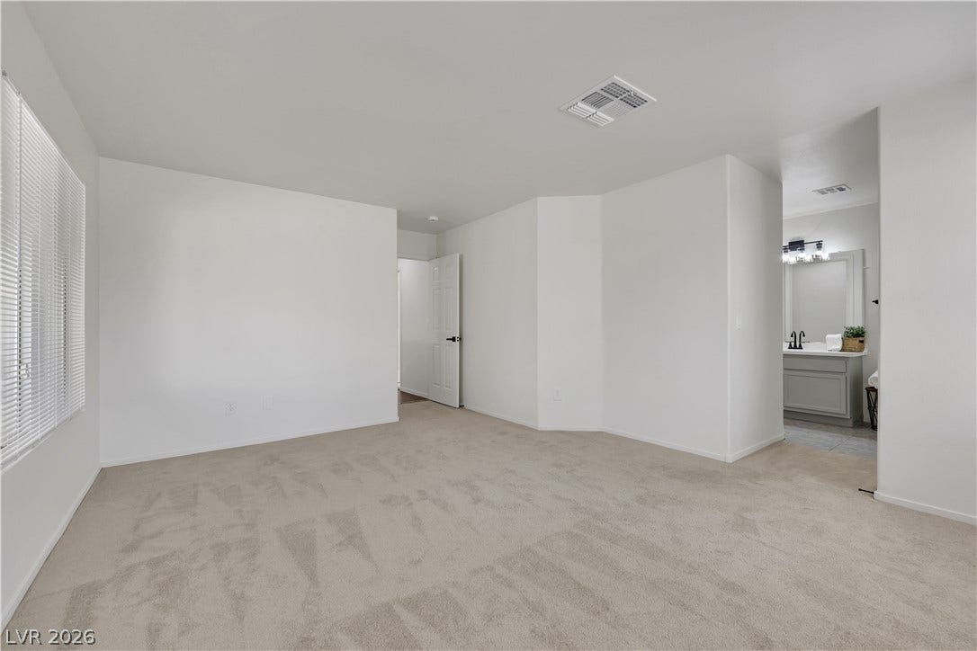 648 Moonlight Mesa Drive, Henderson, NV 89011 A spacious bedroom offers plush carpeting and ample natural light from broad windows, with direct bathroom access.