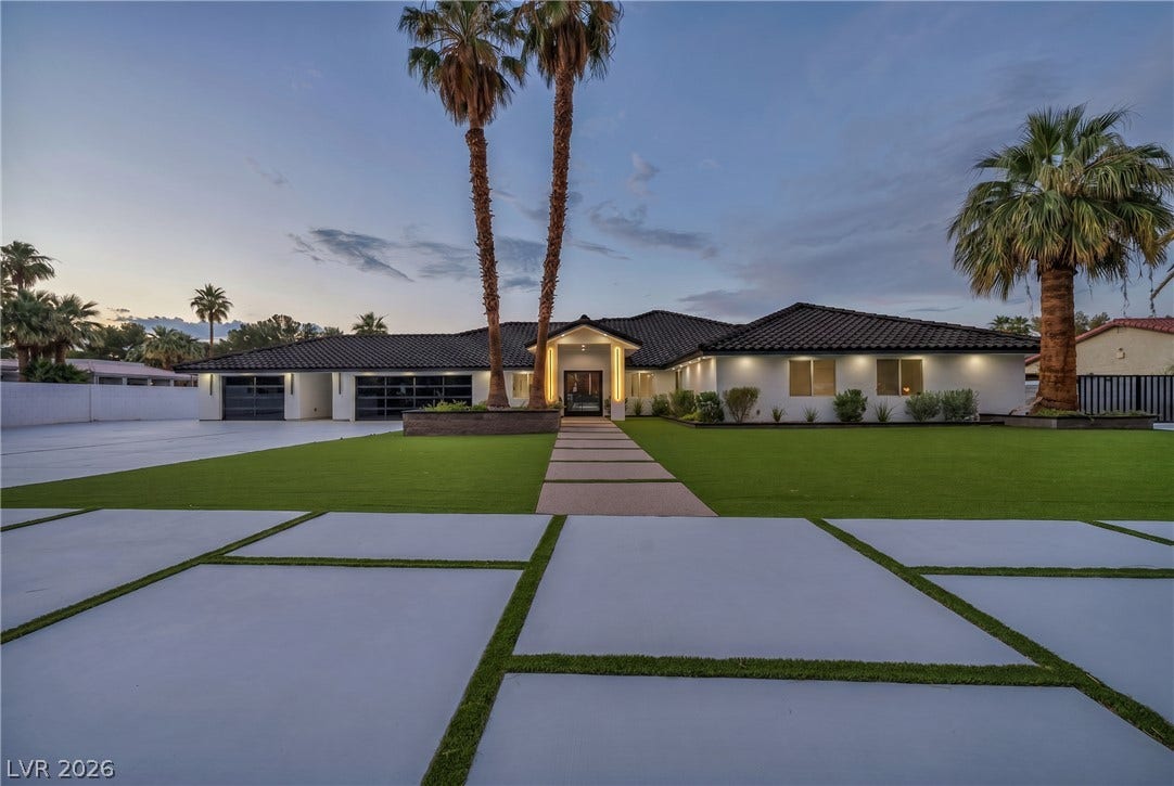 3630 Tobias Lane, Las Vegas, NV 89120 A striking modern facade with contrasting white walls and a dark tile roof, accented by towering palm trees and illuminated pathways.