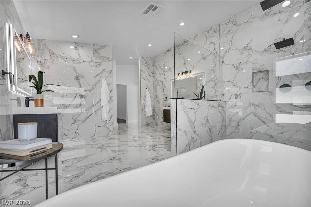 3630 Tobias Lane, Las Vegas, NV 89120 A spacious primary bathroom boasts a freestanding tub and a glass-enclosed shower with pristine marble-patterned tile throughout.
