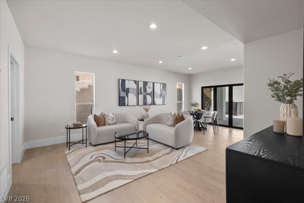 8024 Shorecrest Drive, Las Vegas, NV 89128 Recessed lighting illuminates a spacious living room featuring light hardwood flooring and a dining area beyond.