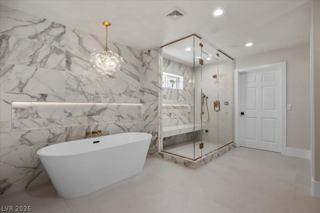8024 Shorecrest Drive, Las Vegas, NV 89128 Marble-clad walls define a luxurious primary bath with a freestanding tub and spacious glass-enclosed shower.